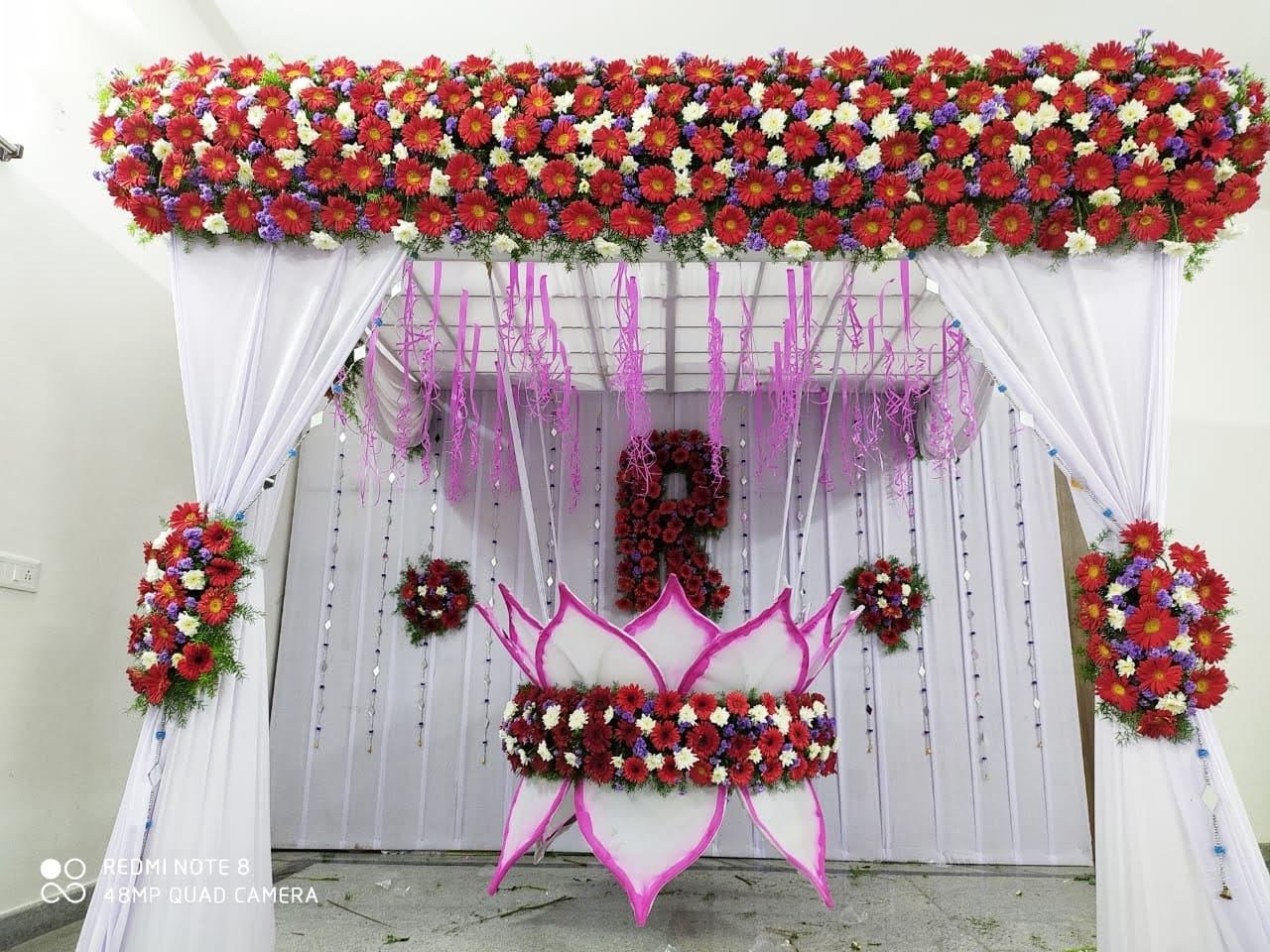 Birthday stage decoration with red floral canopy and monogram