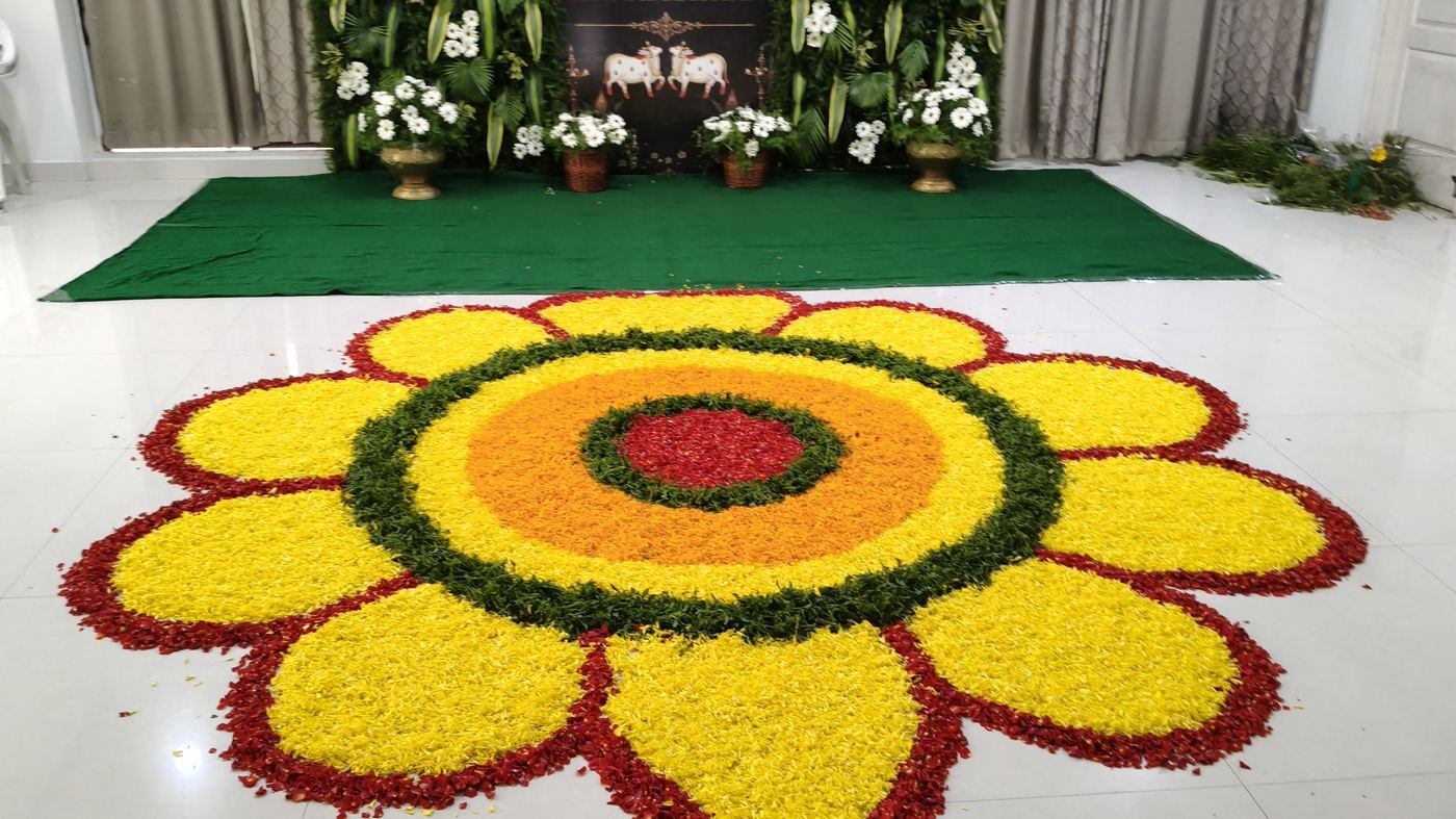 Sunflower shaped flower rangoli floor art in front of a floral mandap backdrop